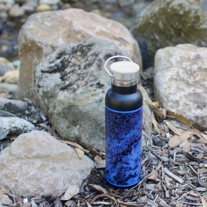 20oz Stainless Steel Insulated Bottle with Bamboo Top in Black with Blue Map next to rocks