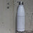 17oz Stainless Steel Insulated Cola Bottle in White with Custom Engraved Map in Front of Concrete Wall