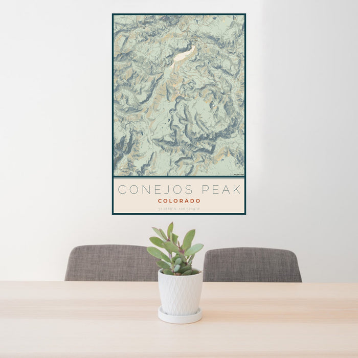 24x36 Conejos Peak Colorado Map Print Portrait Orientation in Woodblock Style Behind 2 Chairs Table and Potted Plant